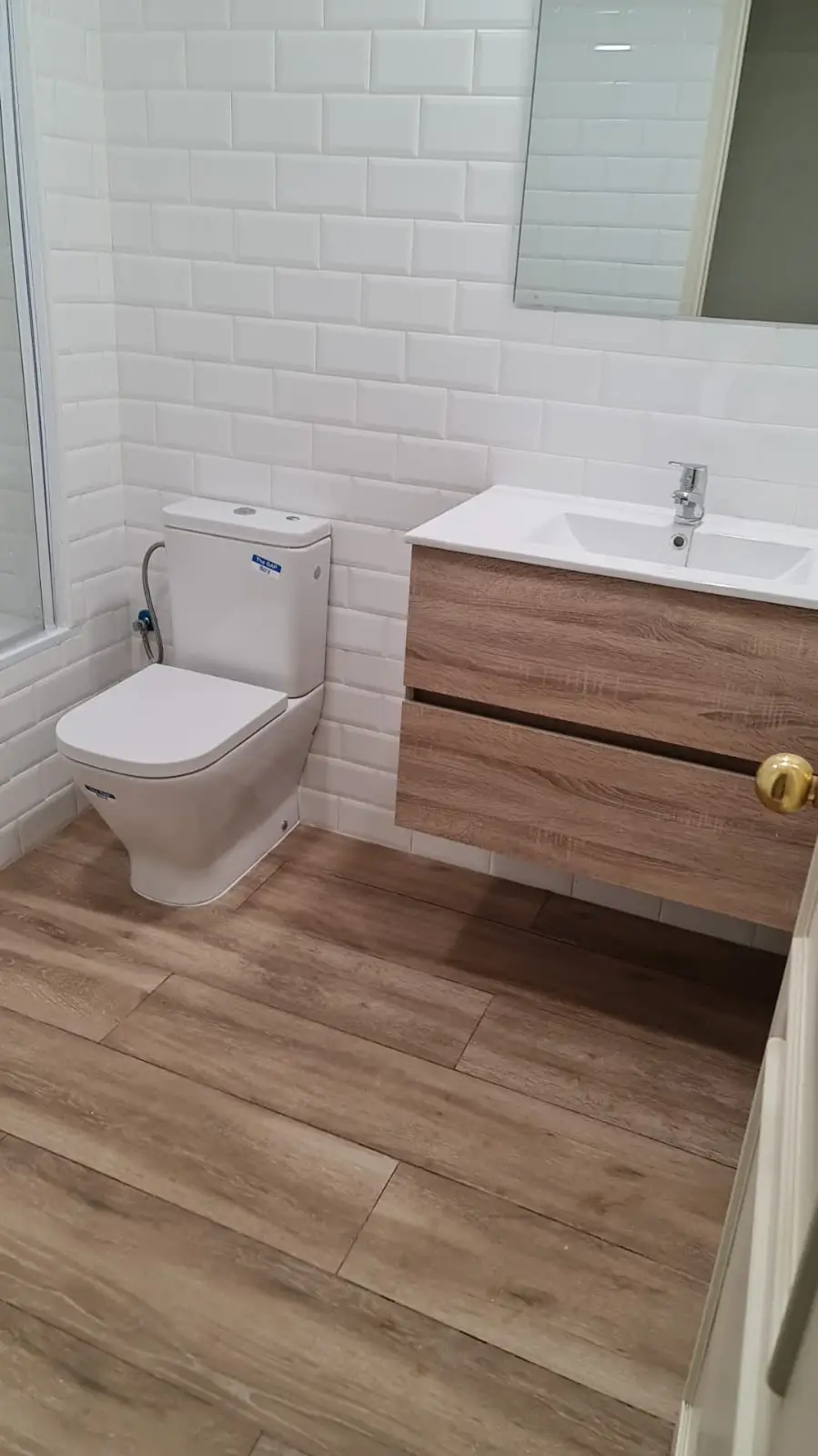 Baño con inodoro, mueble suspendido de madera y azulejo metro blanco