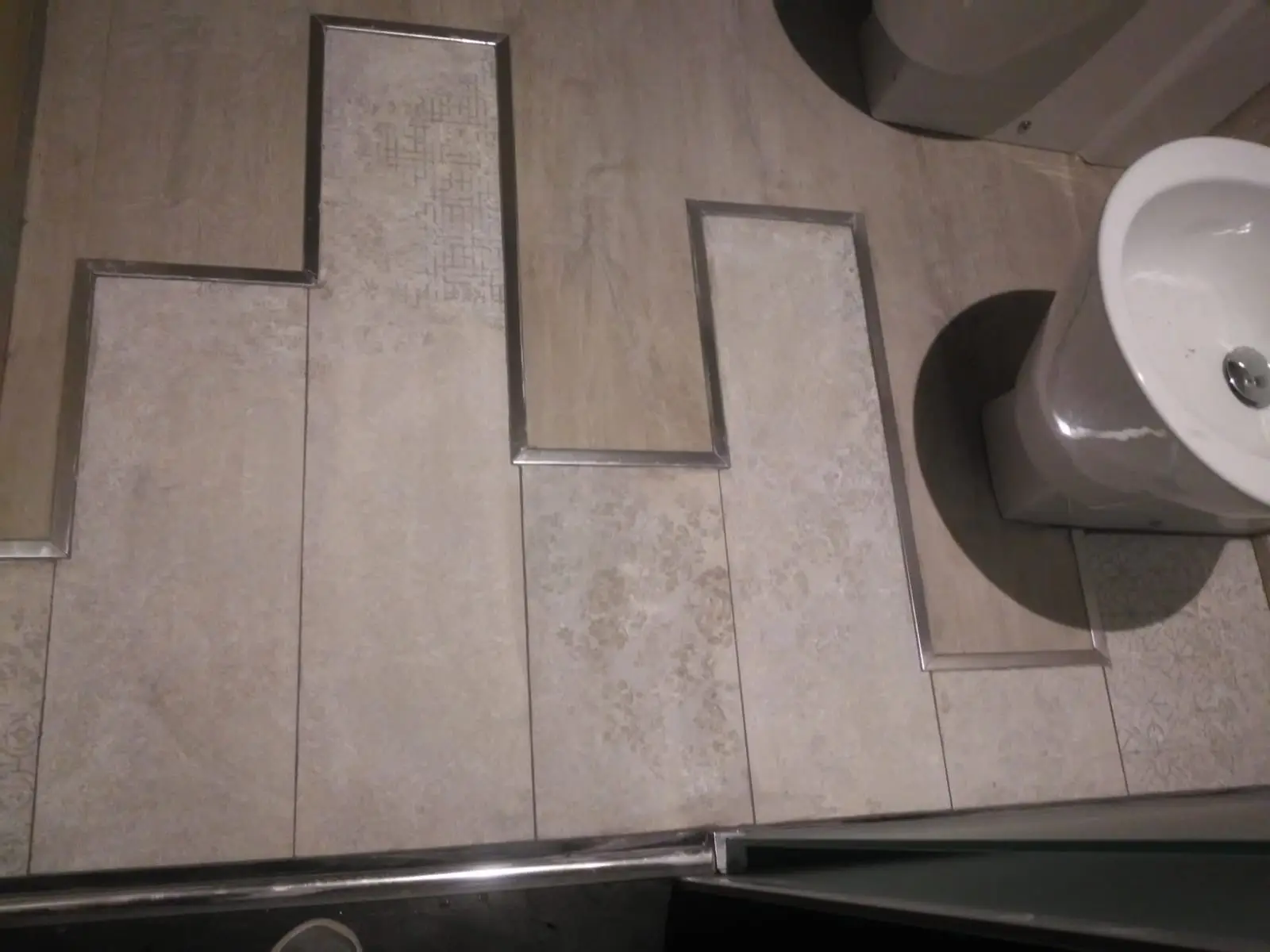 Detalle de suelo de baño con porcelánico decorativo y perfiles metálicos