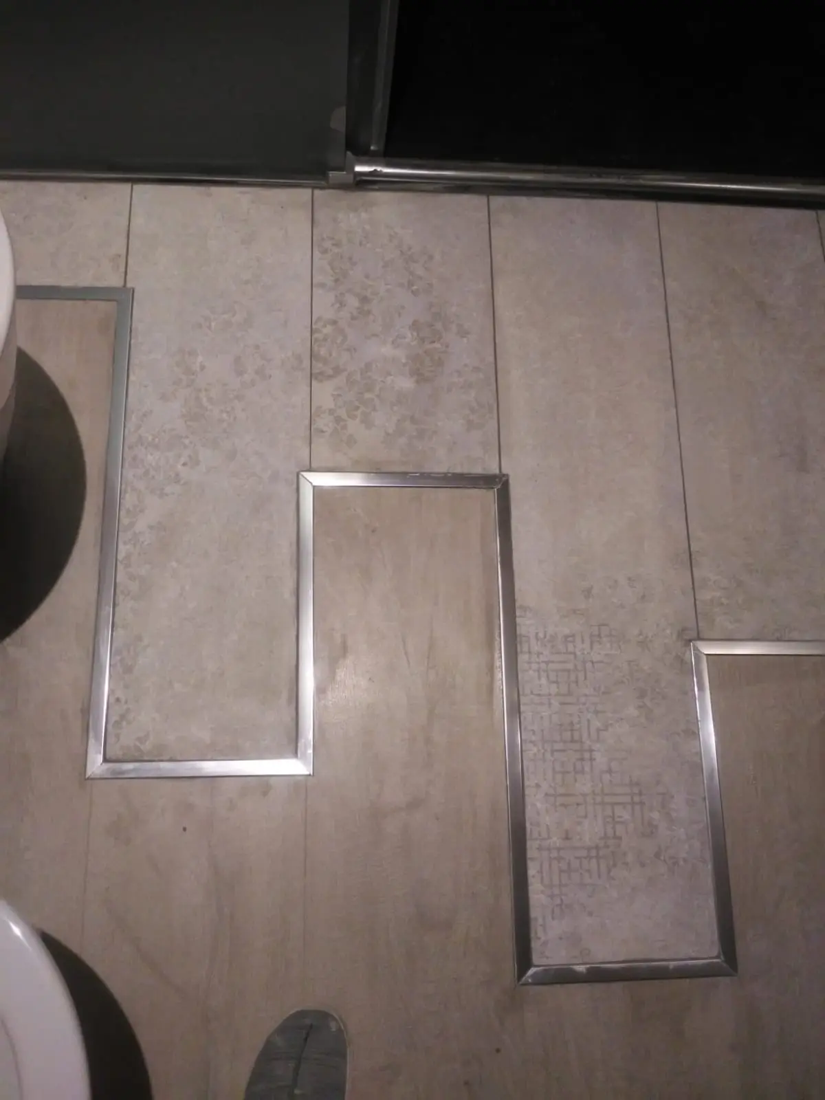 Suelo de baño en porcelánico con diseño de piezas combinadas y perfiles de acero inoxidable