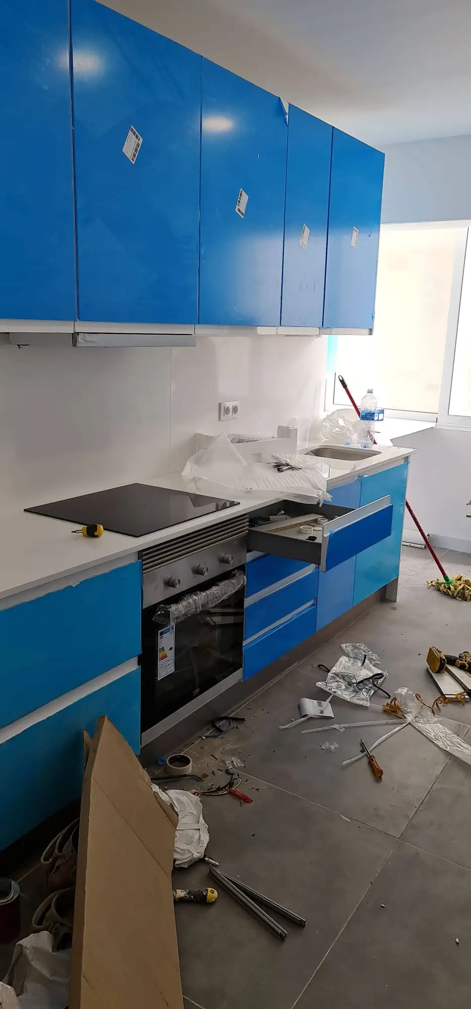 Montaje de cocina con muebles azules brillo, placa de inducción y horno