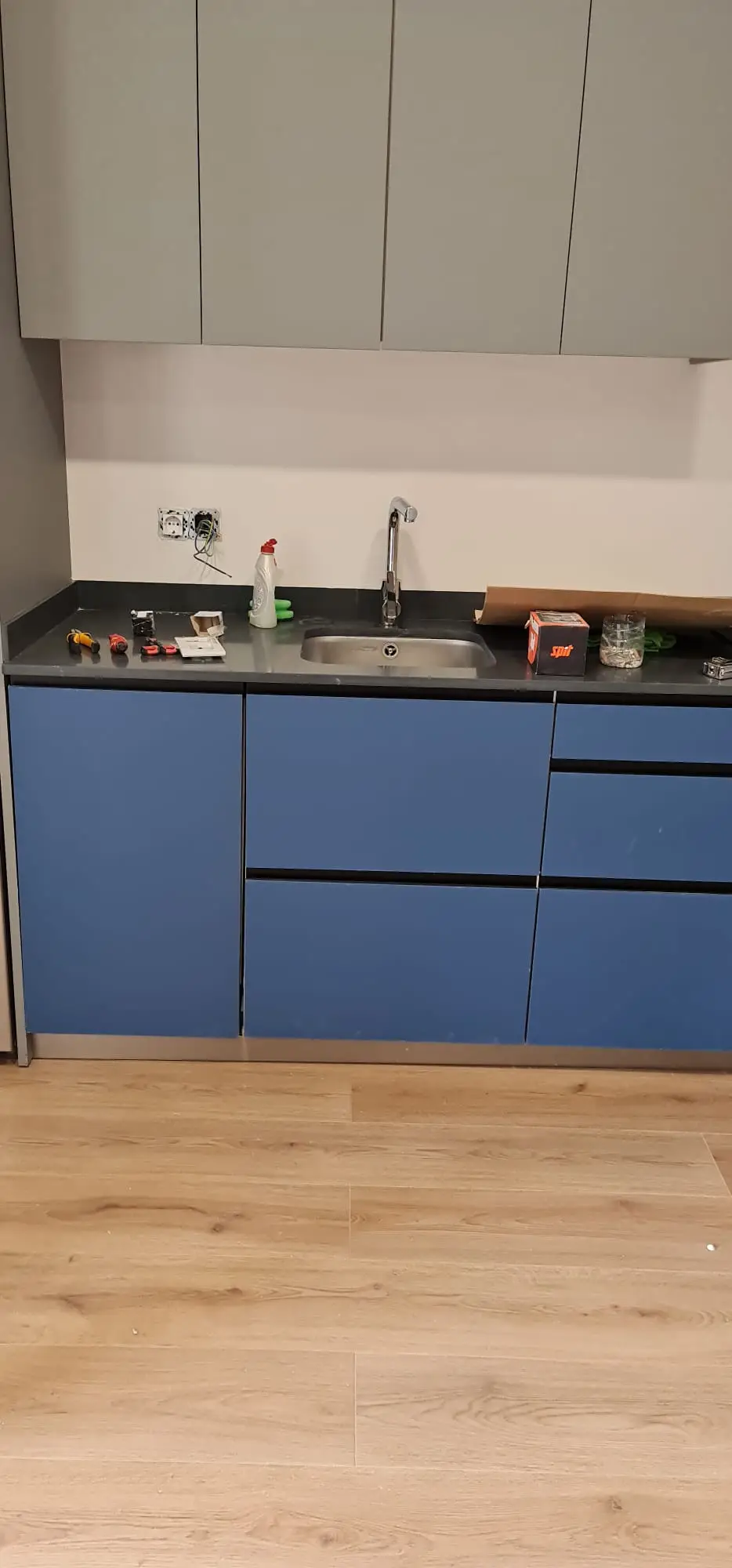 Cocina con muebles azules mate, encimera oscura y suelo laminado de roble