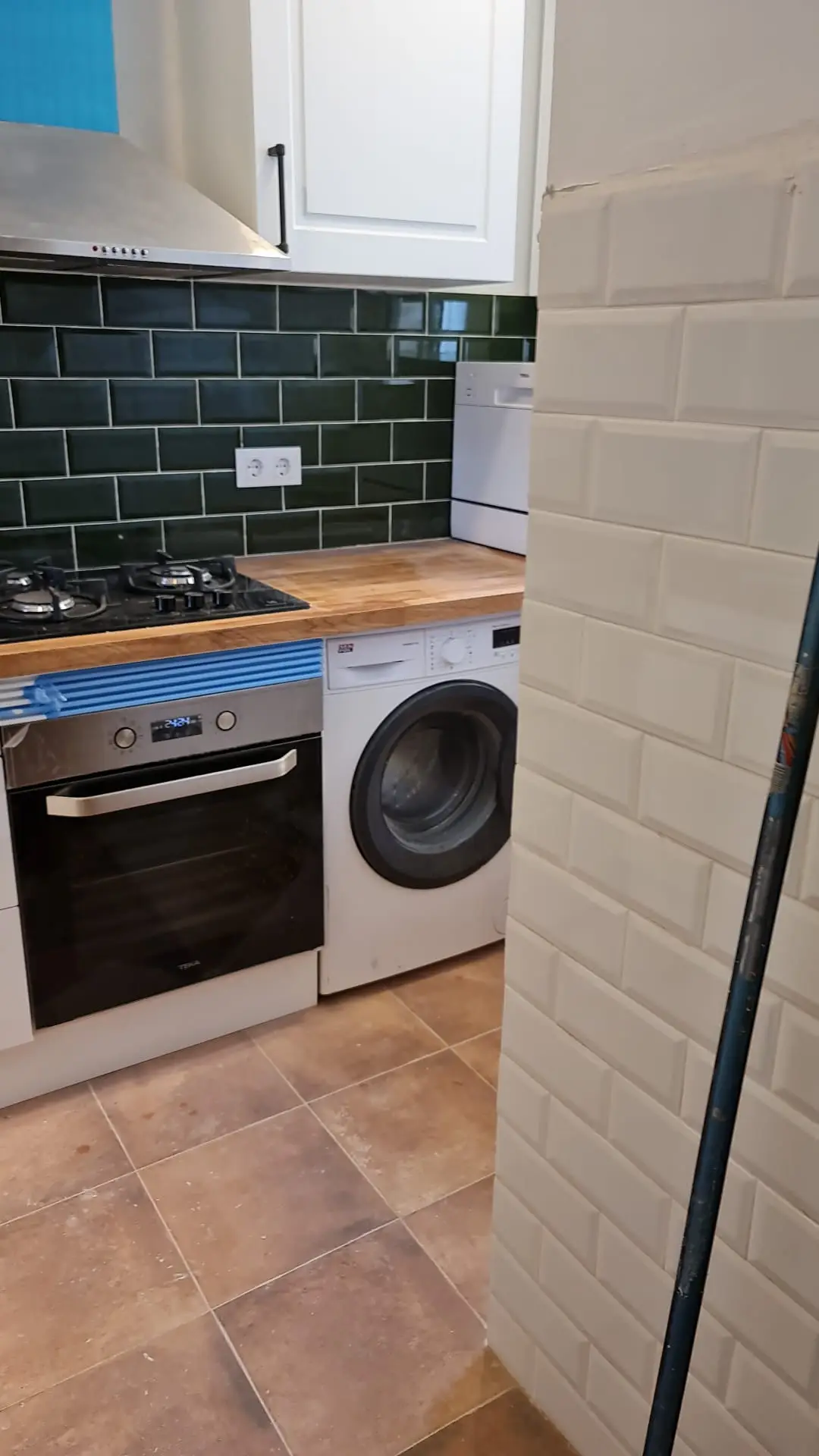 Cocina con encimera de madera, horno, lavadora integrada y azulejo verde