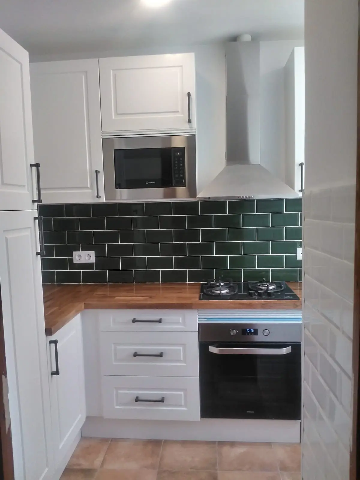 Cocina con muebles blancos de estilo clásico, horno y microondas integrados y azulejo metro verde