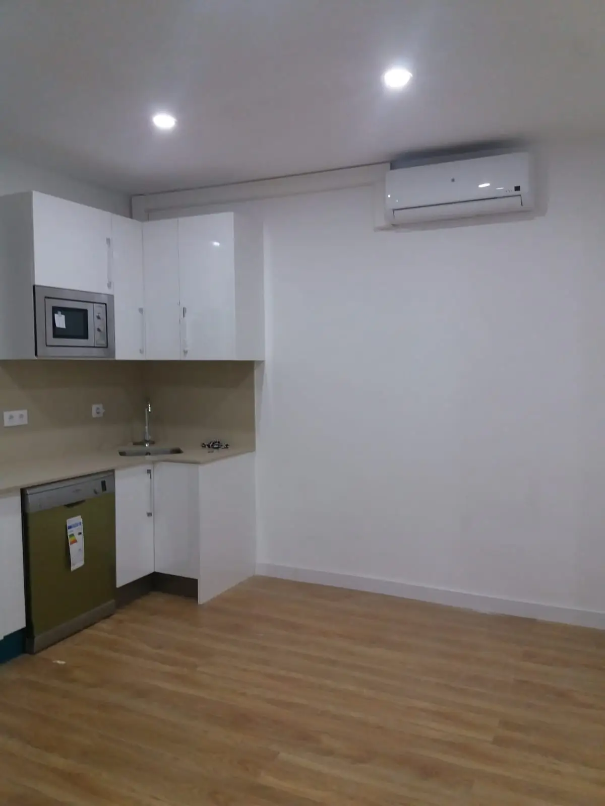 Cocina blanca en L con microondas integrado, aire acondicionado y suelo de madera