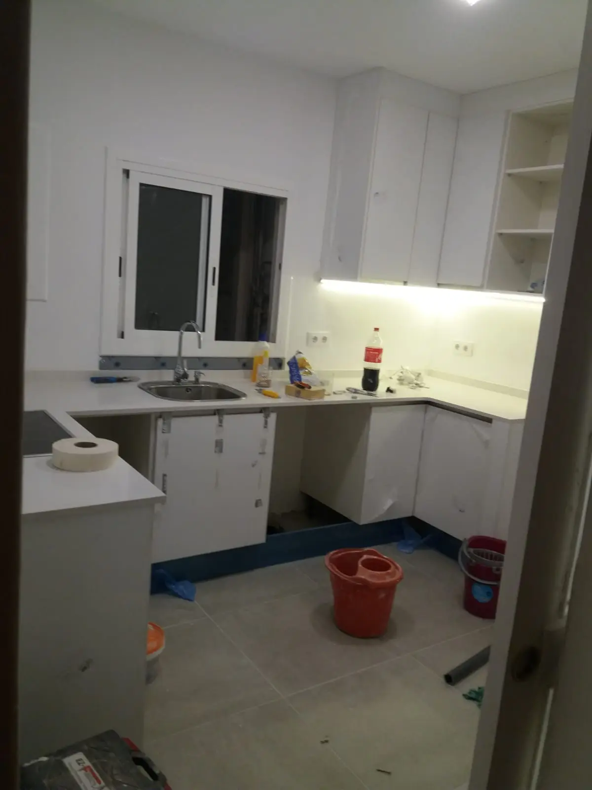 Cocina blanca en U bajo ventana con encimera clara, en fase de montaje