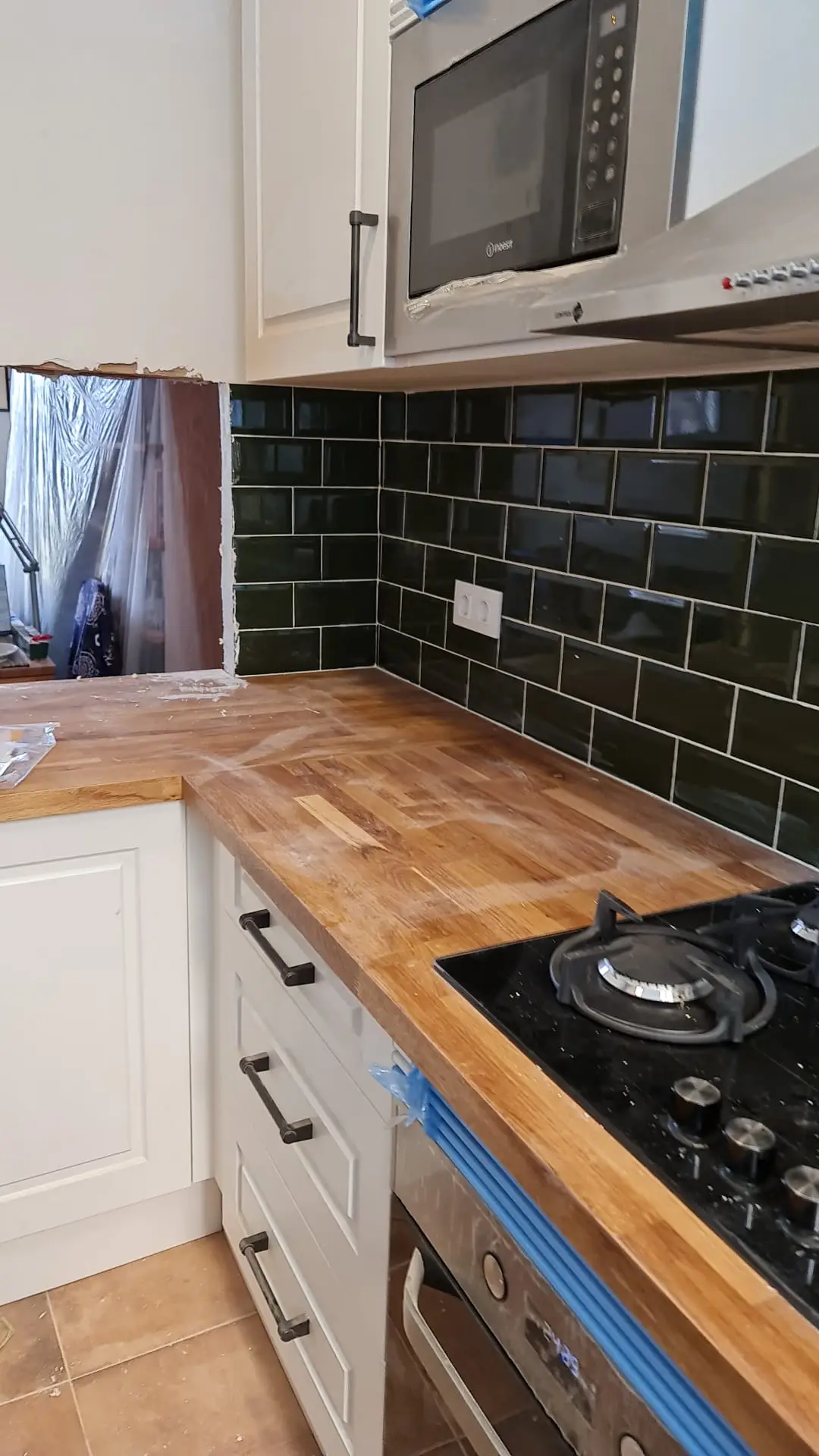 Encimera de madera con placa de gas y azulejo verde durante el montaje de la cocina