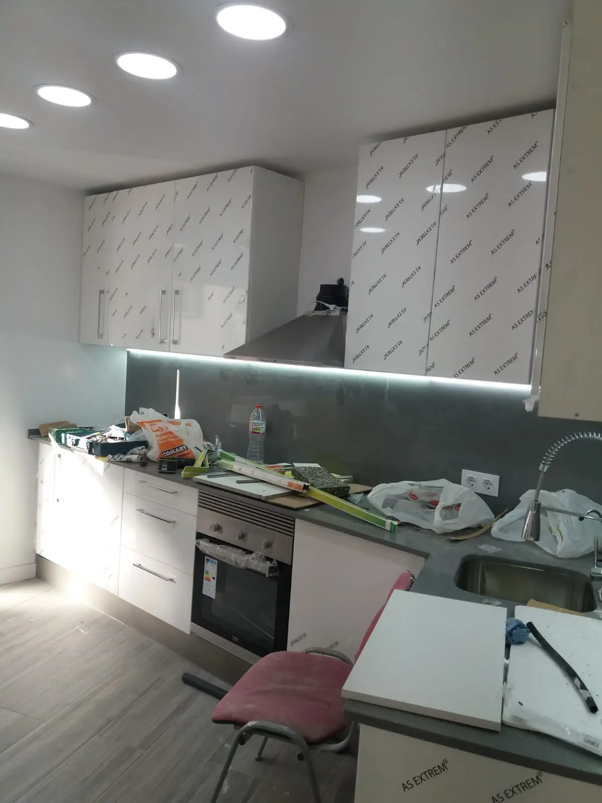 Cocina lineal blanca con tira LED y frente gris durante el montaje
