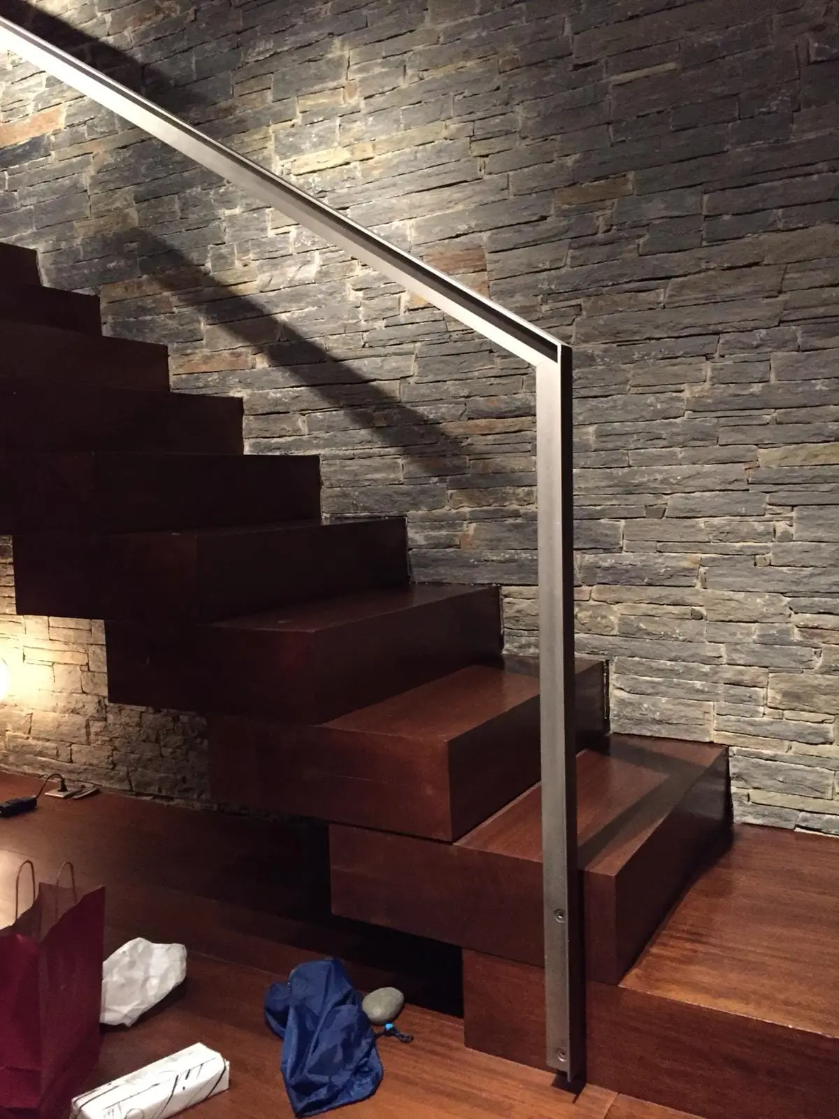 Escalera de madera maciza con barandilla de acero y pared revestida de piedra natural